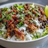 Fork-tender carnitas garnish this hearty burrito bowl, served with sweet corn, zesty lime crema, and chopped cilantro for bright flavor.