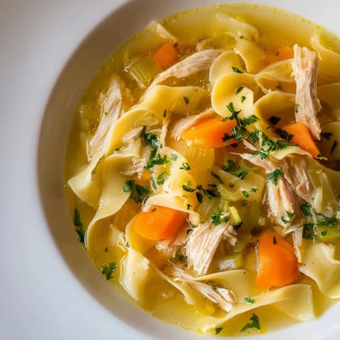 Steaming Chicken Noodle Soup, bright with carrots and parsley, promises warmth in every spoonful.