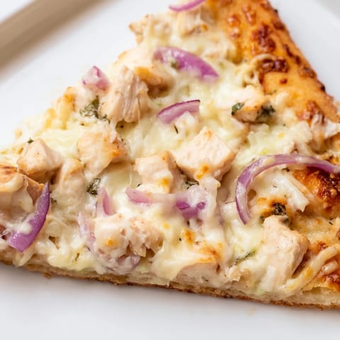 Sliced hot from the oven, Chicken Alfredo Pizza showcases a golden crust, rich white sauce, and savory chicken on a plate.  
