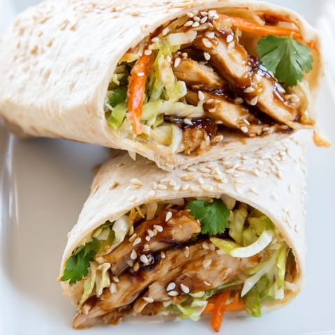 A close-up of a savory Teriyaki Chicken Wrap garnished with sesame seeds and cilantro, perfect for a quick lunch.