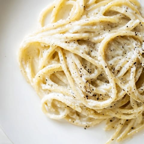 Close-up view of Spaghetti Cacio e Pepe in a skillet, highlighting the silky, emulsified sauce clinging to each strand of pasta.  