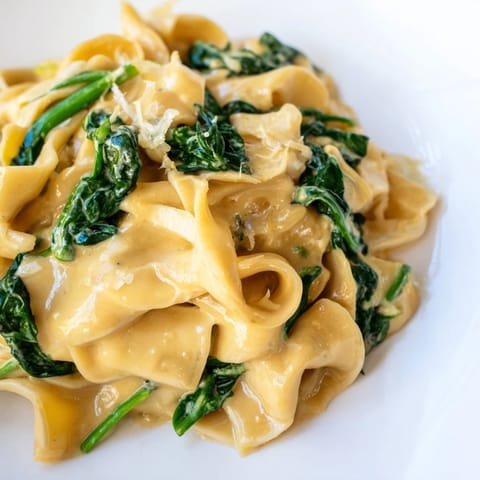 Freshly prepared creamy spinach garlic noodles garnished with shaved Parmesan and red pepper flakes, steaming gently on a rustic wooden table.