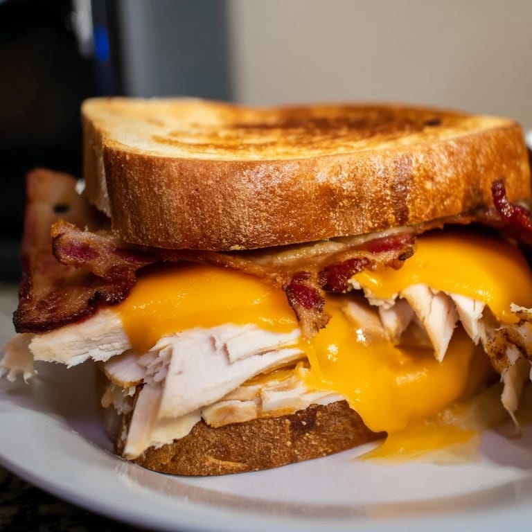 Two halves of a Turkey Club Grilled Cheese stacked on a plate, with melted cheese oozing out.