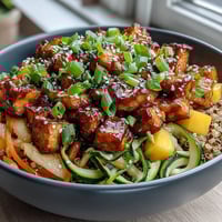 A top-down view of an Easy Teriyaki Quinoa Bowl with baked tofu, spiralized zucchini and carrots, and sweet mango on fluffy quinoa.